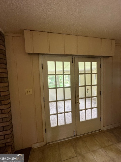 doorway featuring a healthy amount of sunlight, french doors, light tile floors, and a textured ceiling