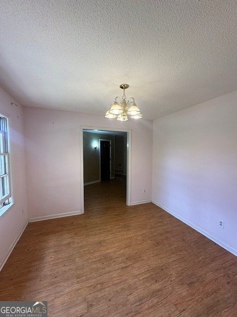 spare room with a notable chandelier, a textured ceiling, and dark hardwood / wood-style flooring