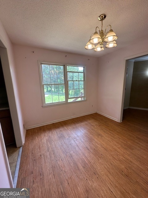 spare room featuring a notable chandelier, wood-type flooring, and a textured ceiling