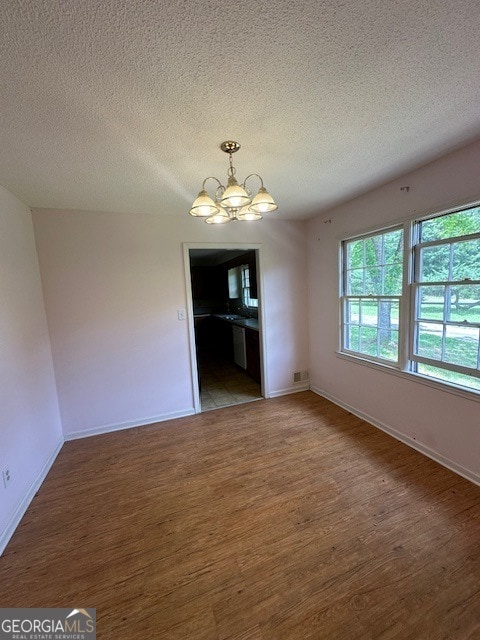 unfurnished room with an inviting chandelier, a textured ceiling, and hardwood / wood-style flooring