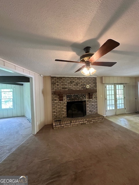 unfurnished living room featuring a textured ceiling, brick wall, a fireplace, carpet, and ceiling fan