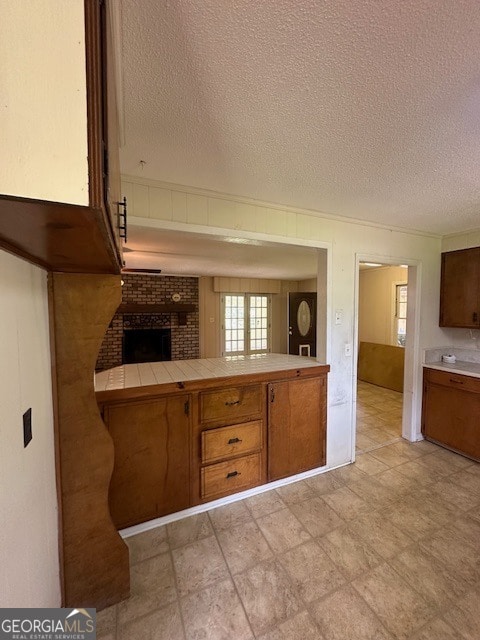 kitchen featuring light tile floors, tile counters, a fireplace, a textured ceiling, and brick wall