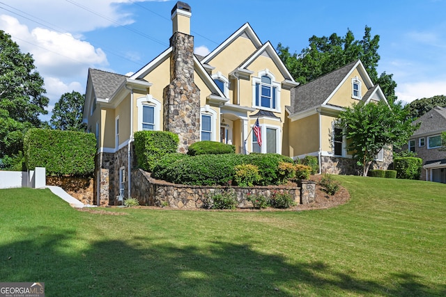 view of front of house with stone siding, a chimney, a front yard, and stucco siding