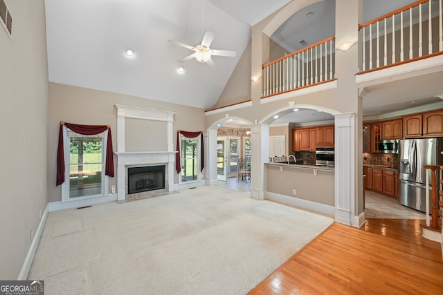 unfurnished living room featuring high vaulted ceiling, ceiling fan, light hardwood / wood-style flooring, and decorative columns