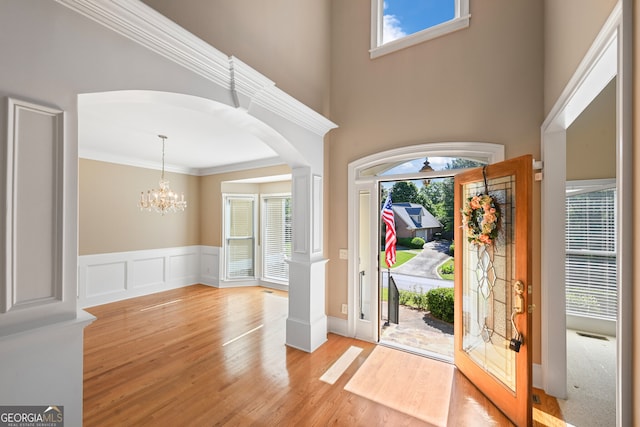 foyer featuring ornamental molding, light hardwood / wood-style flooring, a towering ceiling, and a chandelier