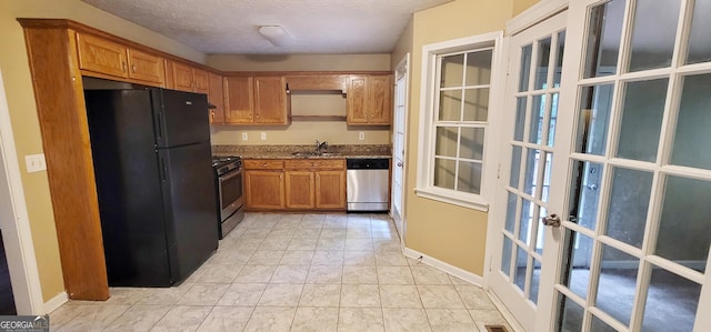 kitchen with a textured ceiling, appliances with stainless steel finishes, french doors, sink, and stone counters