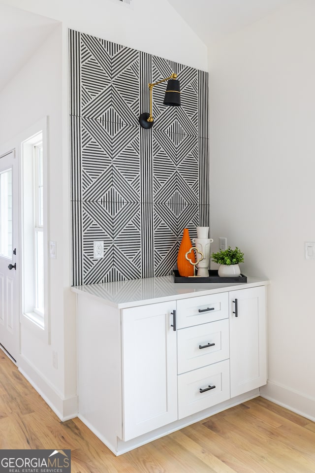 bar with white cabinets and light wood-type flooring