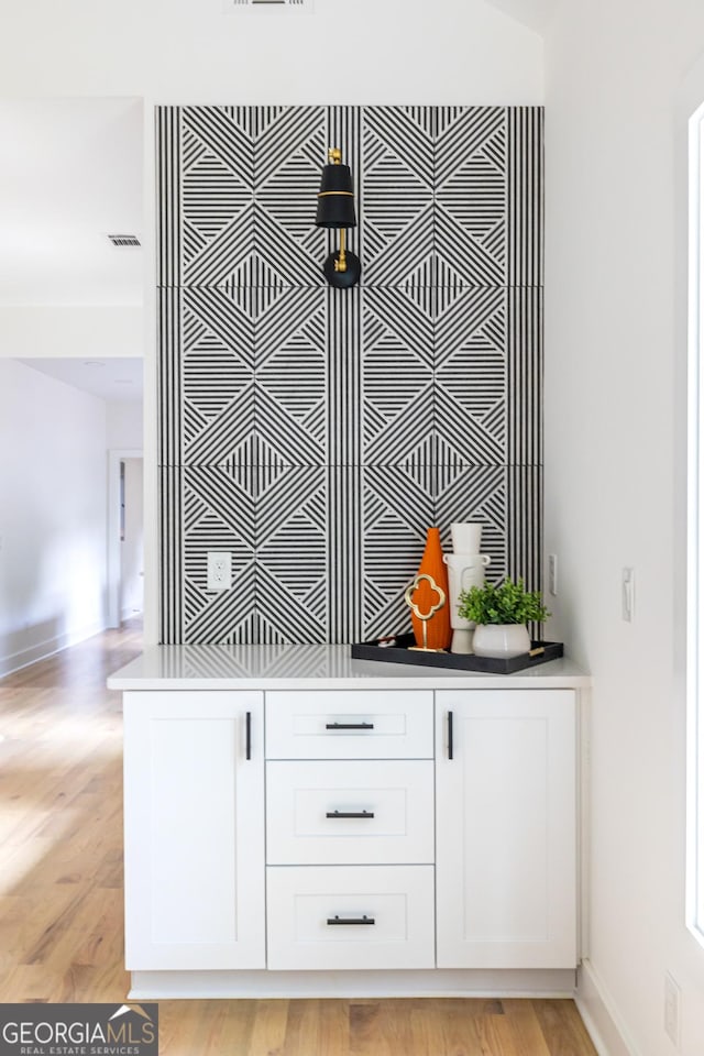 bar with white cabinets and light wood-type flooring