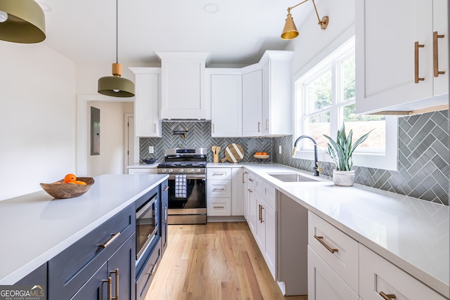 kitchen with light hardwood / wood-style floors, pendant lighting, sink, white cabinets, and appliances with stainless steel finishes