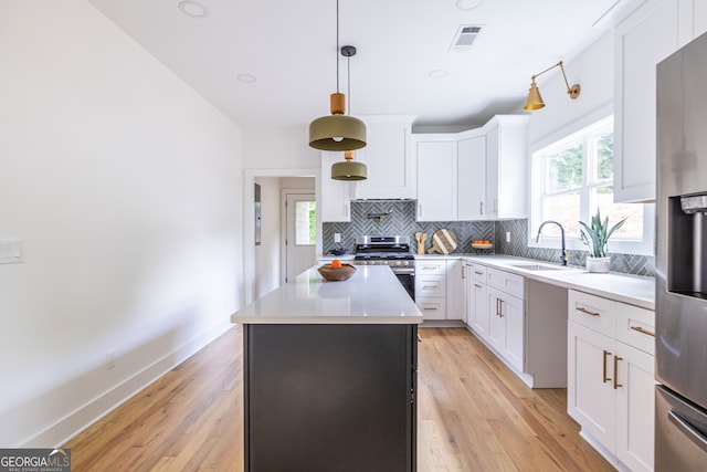 kitchen featuring light wood-type flooring, a kitchen island, backsplash, sink, and appliances with stainless steel finishes