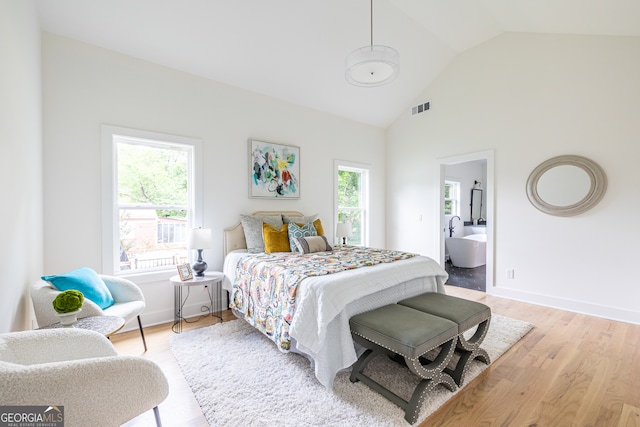 bedroom with high vaulted ceiling, ensuite bathroom, and light wood-type flooring