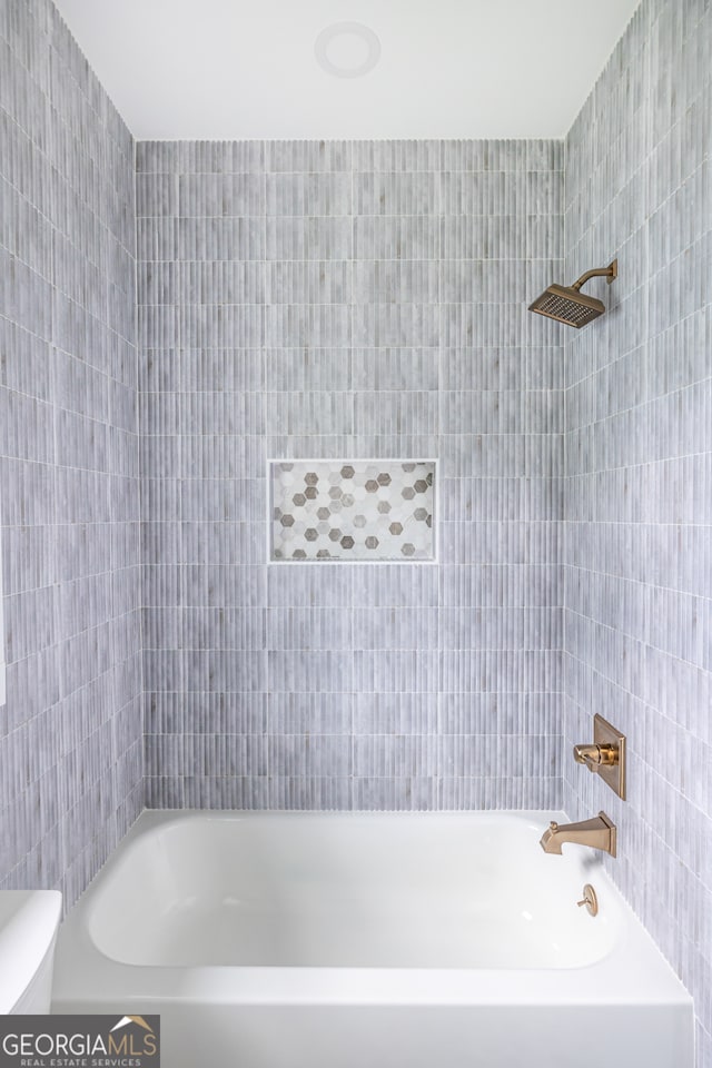 bathroom with tile walls, toilet, and tiled shower / bath