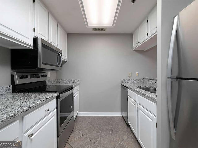 kitchen with stainless steel appliances, white cabinets, light tile floors, and light stone counters