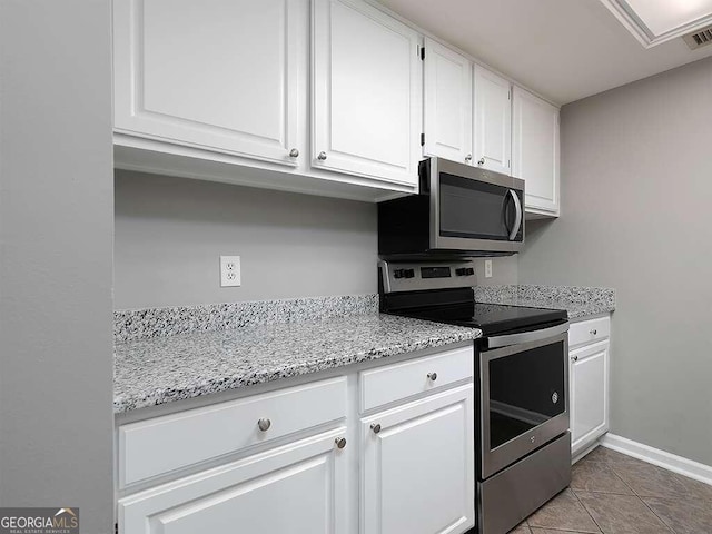 kitchen with appliances with stainless steel finishes, white cabinetry, tile floors, and light stone countertops