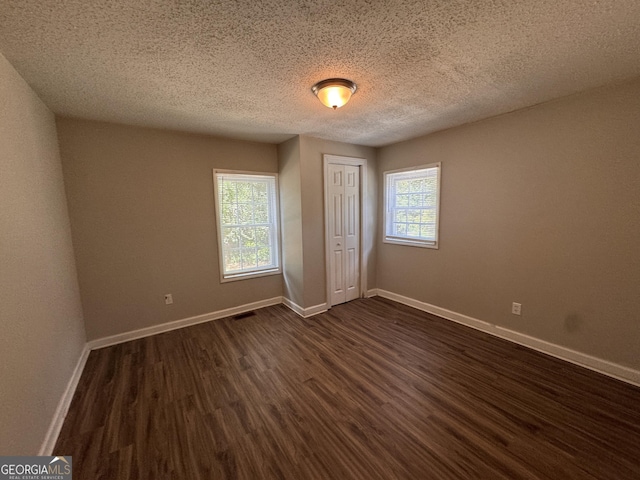 unfurnished bedroom with multiple windows, dark hardwood / wood-style floors, a textured ceiling, and a closet