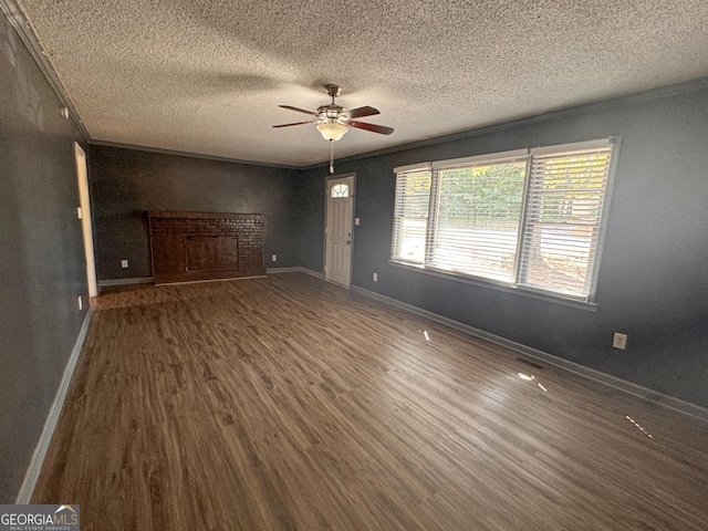 spare room featuring crown molding, ceiling fan, a fireplace, a textured ceiling, and dark hardwood / wood-style flooring