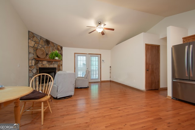 living room with light wood-type flooring, lofted ceiling, ceiling fan, and a fireplace