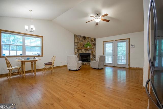 living room featuring a stone fireplace, light hardwood / wood-style flooring, french doors, ceiling fan with notable chandelier, and lofted ceiling