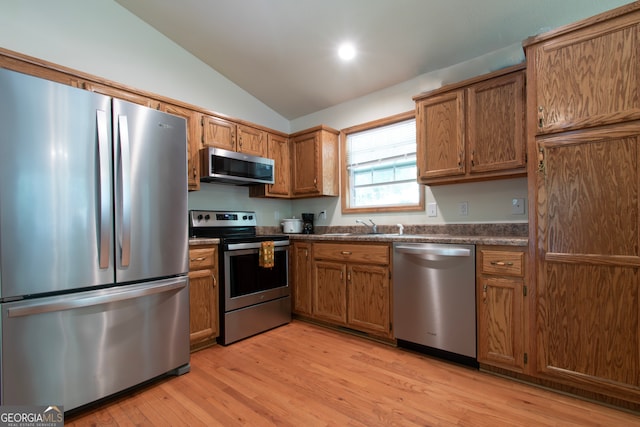 kitchen featuring appliances with stainless steel finishes, light hardwood / wood-style floors, sink, and vaulted ceiling