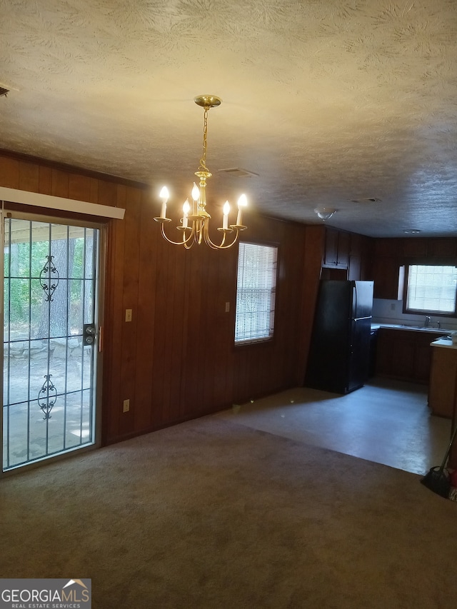 unfurnished dining area featuring a notable chandelier, a textured ceiling, dark colored carpet, wood walls, and sink