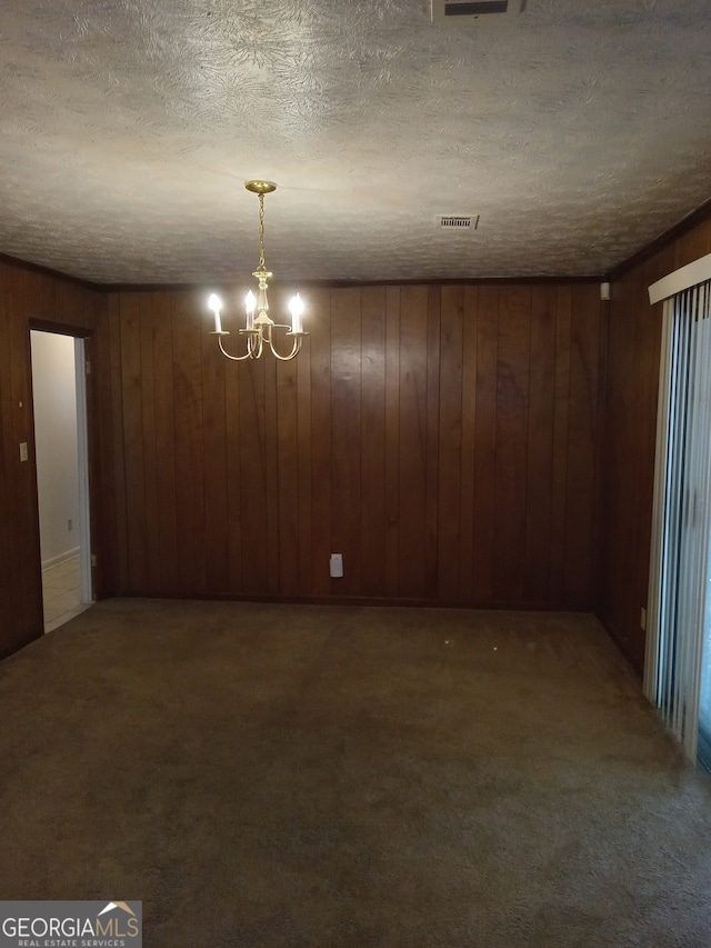 unfurnished room featuring wood walls, dark colored carpet, a textured ceiling, and a chandelier