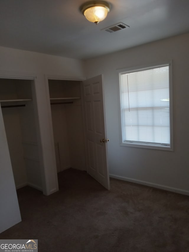 unfurnished bedroom featuring two closets and dark carpet