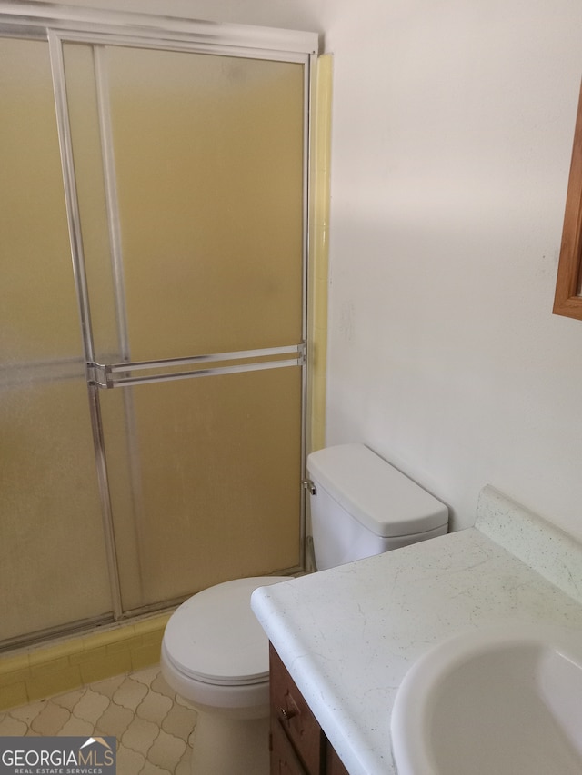 bathroom with tile flooring, a shower with shower door, toilet, and vanity