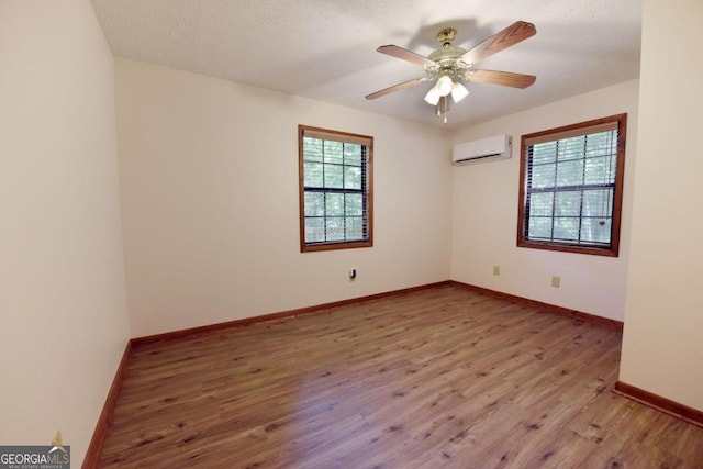 empty room with an AC wall unit, plenty of natural light, ceiling fan, and hardwood / wood-style floors