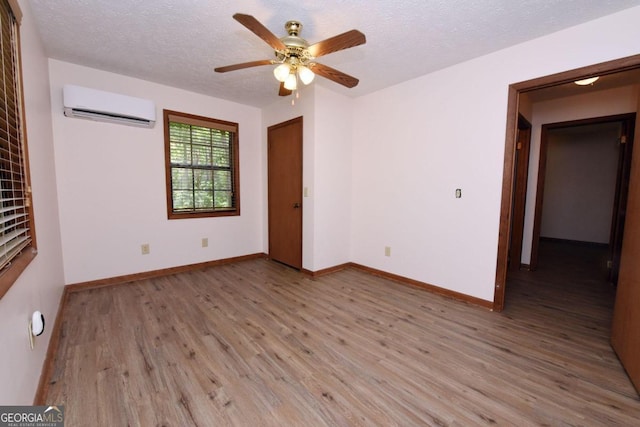 empty room featuring ceiling fan, hardwood / wood-style flooring, a textured ceiling, and a wall mounted air conditioner