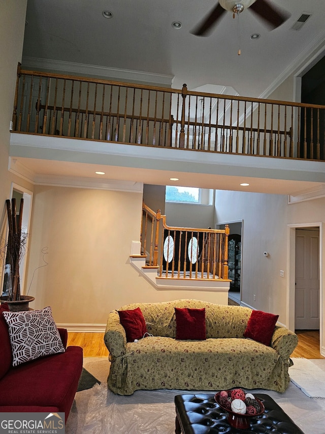 living area featuring visible vents, ceiling fan, stairway, a towering ceiling, and wood finished floors