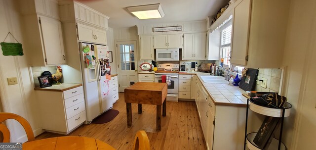 kitchen with light hardwood / wood-style floors, white appliances, white cabinets, tile countertops, and backsplash