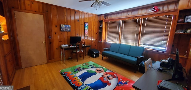 home office featuring light wood-type flooring, wooden walls, and ceiling fan