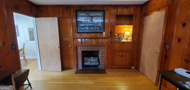 living room featuring wood walls, light wood-type flooring, and a brick fireplace