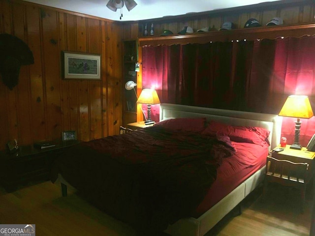 bedroom with ceiling fan, wood walls, and wood-type flooring