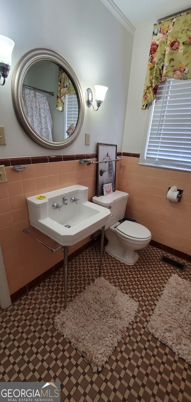 bathroom featuring tile flooring, ornamental molding, toilet, and tile walls