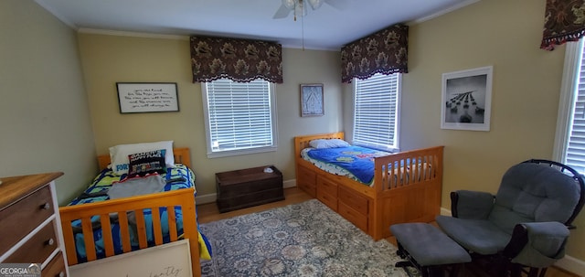 bedroom featuring multiple windows, ornamental molding, ceiling fan, and hardwood / wood-style floors