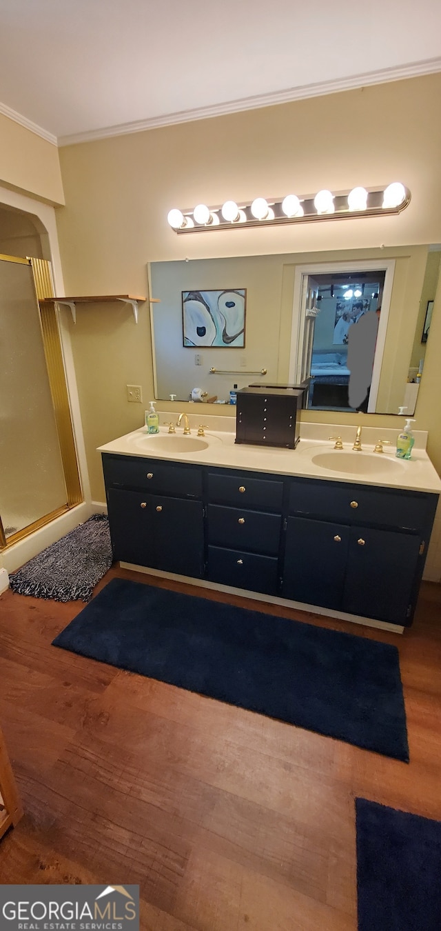 bathroom featuring dual bowl vanity, ornamental molding, wood-type flooring, and a shower with door