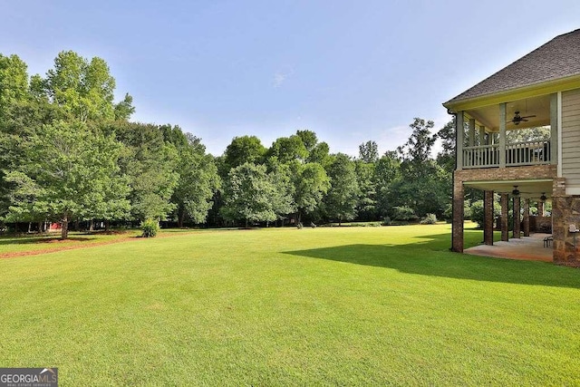 view of green lawn featuring a ceiling fan, a patio, and a balcony