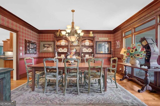 dining area with ornamental molding, an inviting chandelier, and light hardwood / wood-style floors