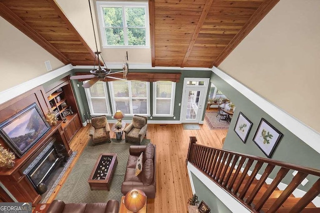 living room featuring wood finished floors, wooden ceiling, a ceiling fan, a fireplace, and high vaulted ceiling