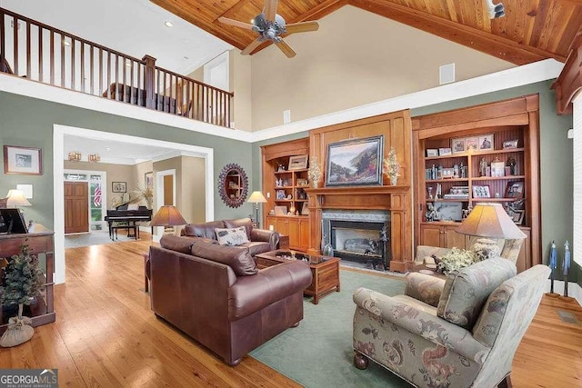 living room with high vaulted ceiling, a ceiling fan, a high end fireplace, wood finished floors, and built in features