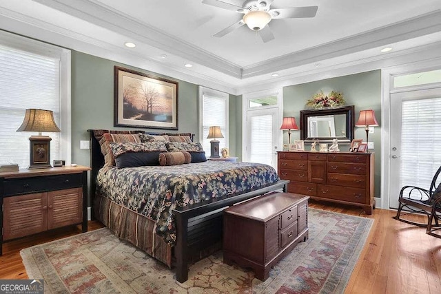 bedroom with crown molding, light wood-style floors, multiple windows, a raised ceiling, and recessed lighting