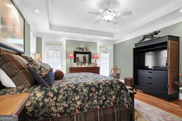 bedroom with light wood-type flooring, a raised ceiling, crown molding, and ceiling fan