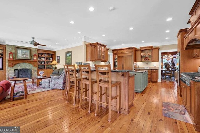 kitchen featuring a breakfast bar, ceiling fan, a stone fireplace, and light hardwood / wood-style floors