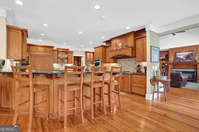 kitchen featuring a kitchen breakfast bar, oven, paneled refrigerator, light hardwood / wood-style flooring, and ornamental molding