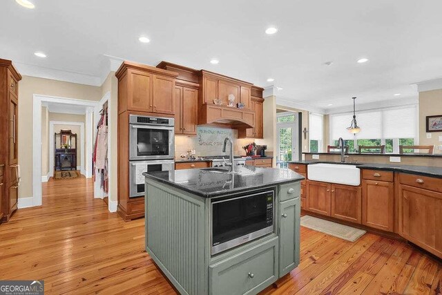 kitchen featuring light hardwood / wood-style flooring, stainless steel appliances, decorative light fixtures, an island with sink, and sink