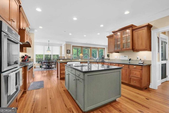 kitchen with dark stone countertops, light hardwood / wood-style flooring, sink, hanging light fixtures, and a center island with sink