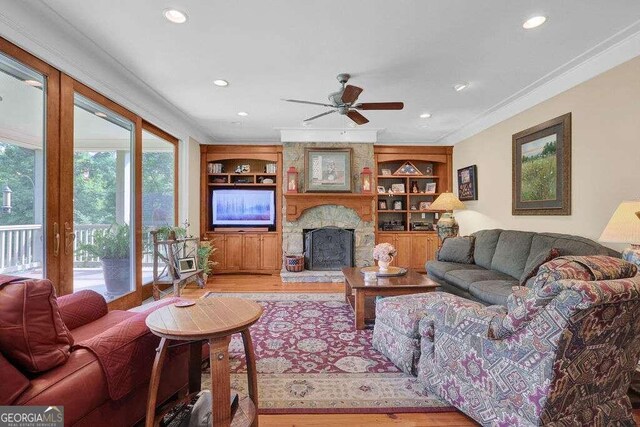 living room with a fireplace, built in features, ornamental molding, ceiling fan, and light wood-type flooring