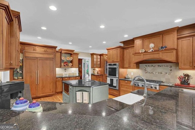 kitchen with light wood-type flooring, a kitchen island with sink, dark stone countertops, sink, and appliances with stainless steel finishes