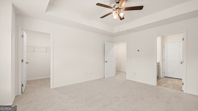 unfurnished bedroom with ceiling fan, a closet, a raised ceiling, a walk in closet, and light colored carpet